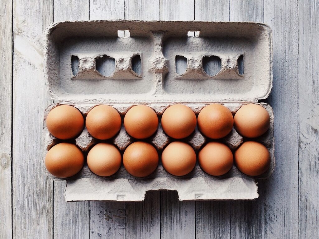 a carton of 12 brown eggs on a wood table.